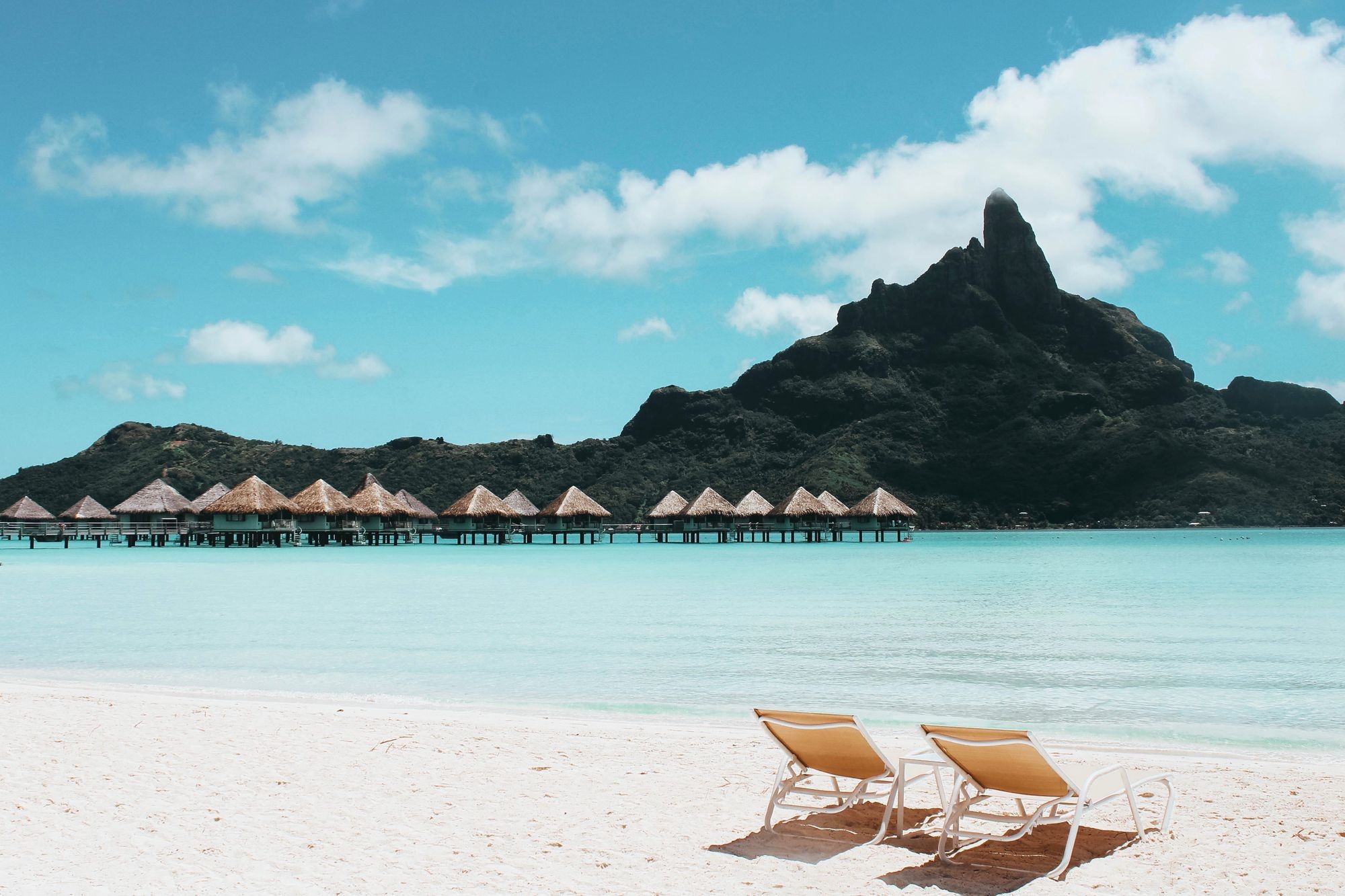 Beach loungers overlooking clear water and a mountain island